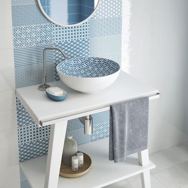 Baño con azulejos con dibujos azules, lavabo redondo con diseño azul, tocador blanco y toalla gris.