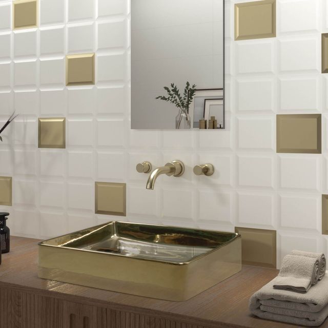 Baño con azulejos texturizados blancos y detalles dorados, que cuenta con lavabo y grifo dorados.