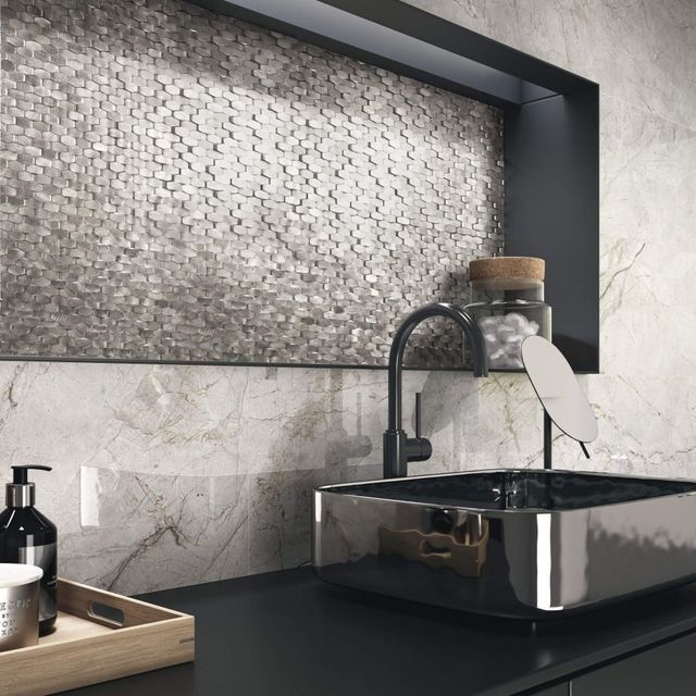 Baño moderno con lavabo cromado, grifo negro, paredes de mármol y salpicadero de mosaico.