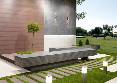 Moderna zona de estar al aire libre con bancos de piedra, césped y árboles.