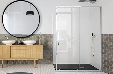 Baño moderno con ducha con marco negro, tocador flotante de madera, espejo circular, paredes grises y un inodoro blanco.