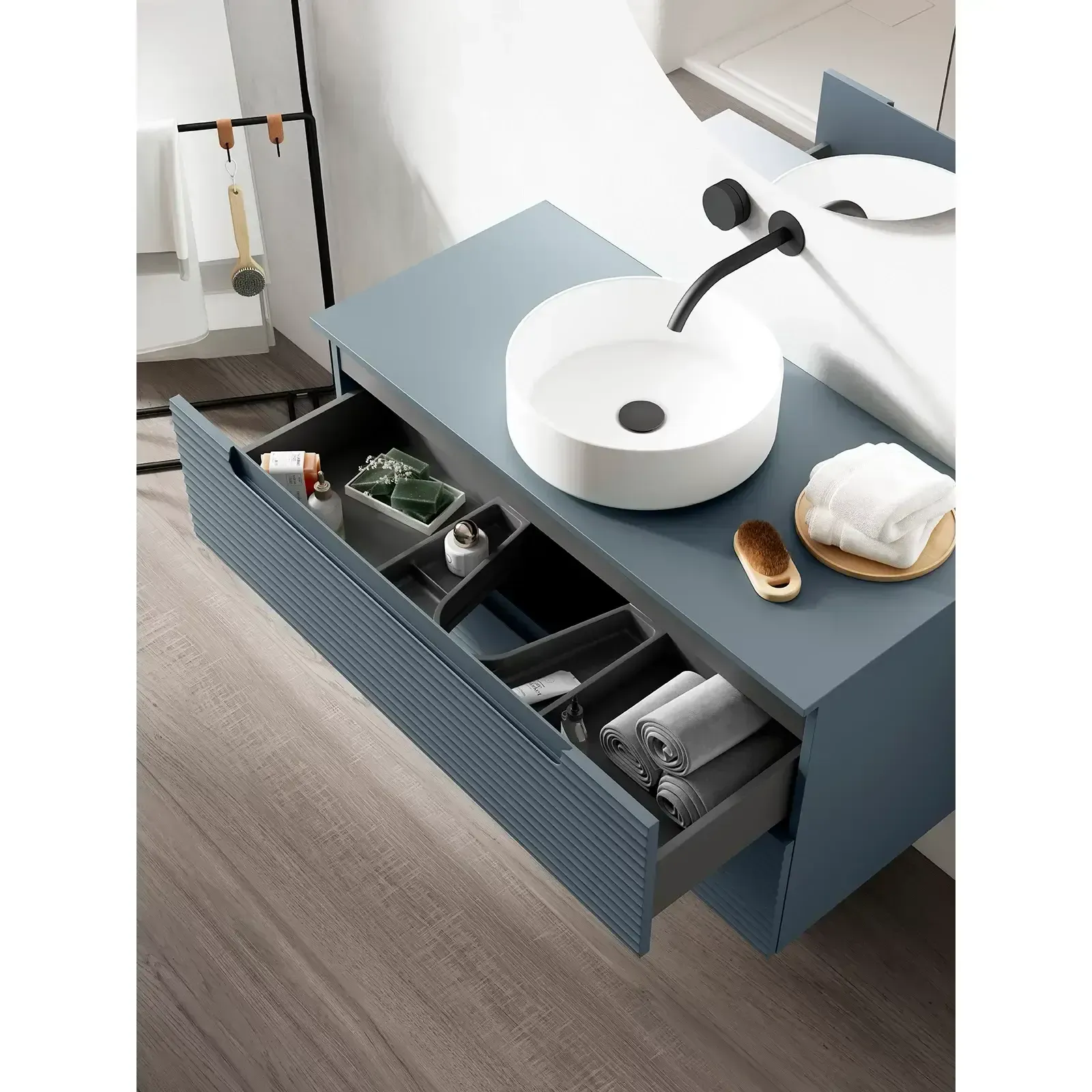 Tocador flotante azul con cajones abiertos, lavabo redondo y toalla, junto a una cama.