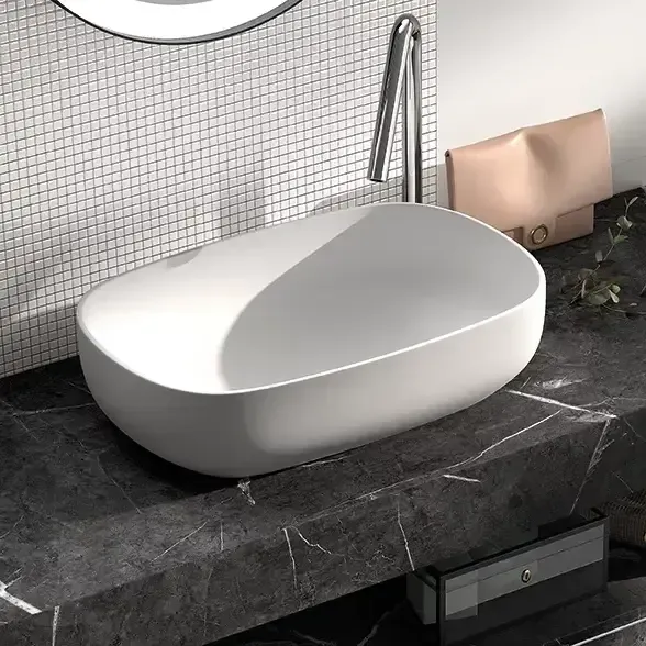 Lavabo ovalado blanco sobre encimera de mármol oscuro con grifo plateado.