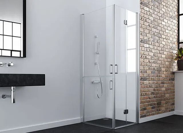 Mampara de ducha en baño con pared de ladrillo y lavabo negro.