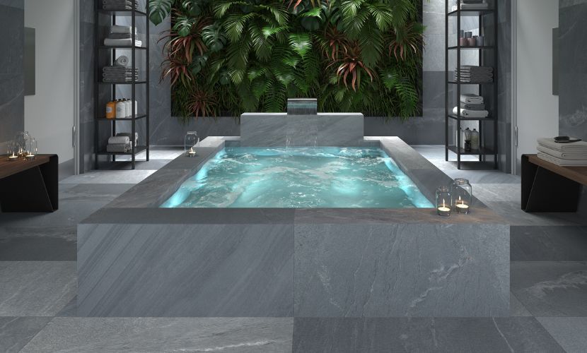 Lujoso baño spa con gran bañera rectangular, paredes de piedra y una pared de planta verde.