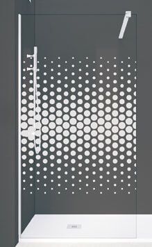 Mampara de ducha con estampado de lunares blancos sobre cristal, sobre pared gris.