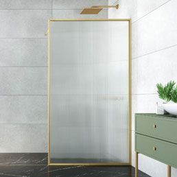 Mampara de ducha con marco dorado en un baño con azulejos gris pálido. Cerca hay un armario verde.