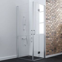 Mampara de ducha de cristal con marco plateado sobre pared de ladrillo y pared blanca. Base de ducha negra.