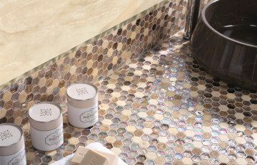 Primer plano de un mostrador de baño con mosaicos hexagonales, frascos pequeños, jabón y un lavabo oscuro.