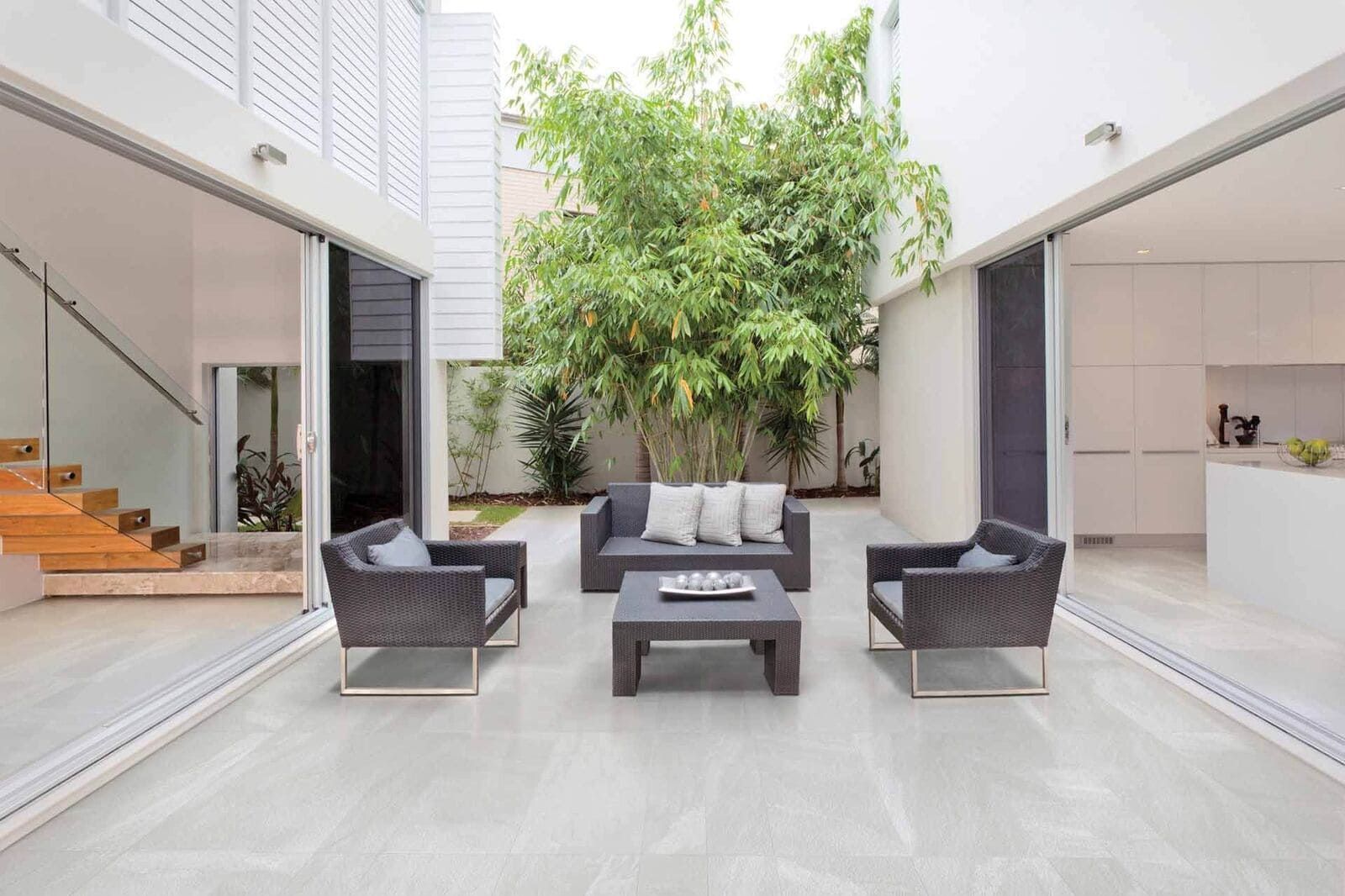 Patio con muebles modernos, exuberante vegetación y puertas corredizas abiertas a espacios interiores.