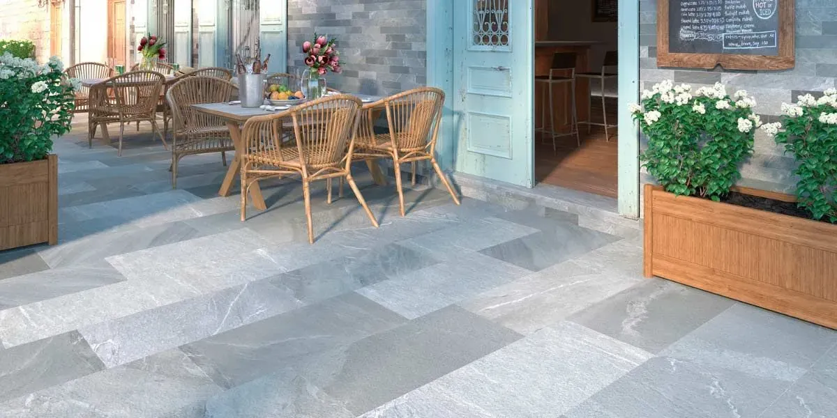 Patio exterior con mesas y sillas, suelo de losas y plantas en macetas.