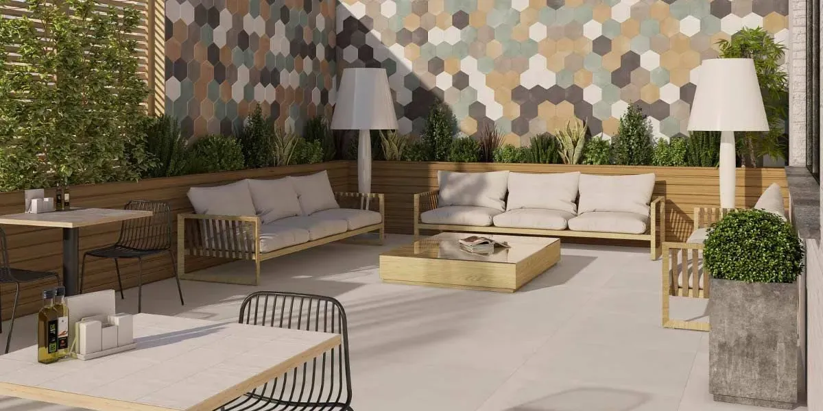 Zona de estar al aire libre con sofás, mesas y pared con diseño hexagonal.