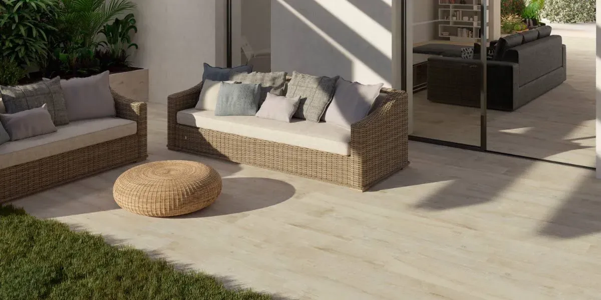 Patio al aire libre con sofás tejidos, otomana redonda y zona de césped.