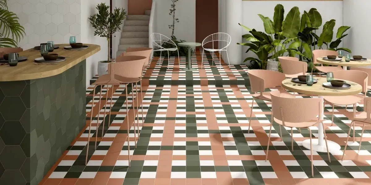 Interior de restaurante con suelo de baldosas, barra, mesas y sillas color melocotón. Plantas y escaleras al fondo.