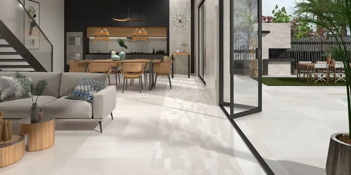 Un interior moderno con puertas abiertas a un patio. El espacio cuenta con suelos claros y una cocina oscura.