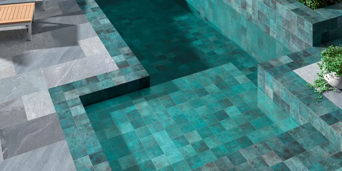 Piscina con azulejos color verde azulado y patio de piedra gris.