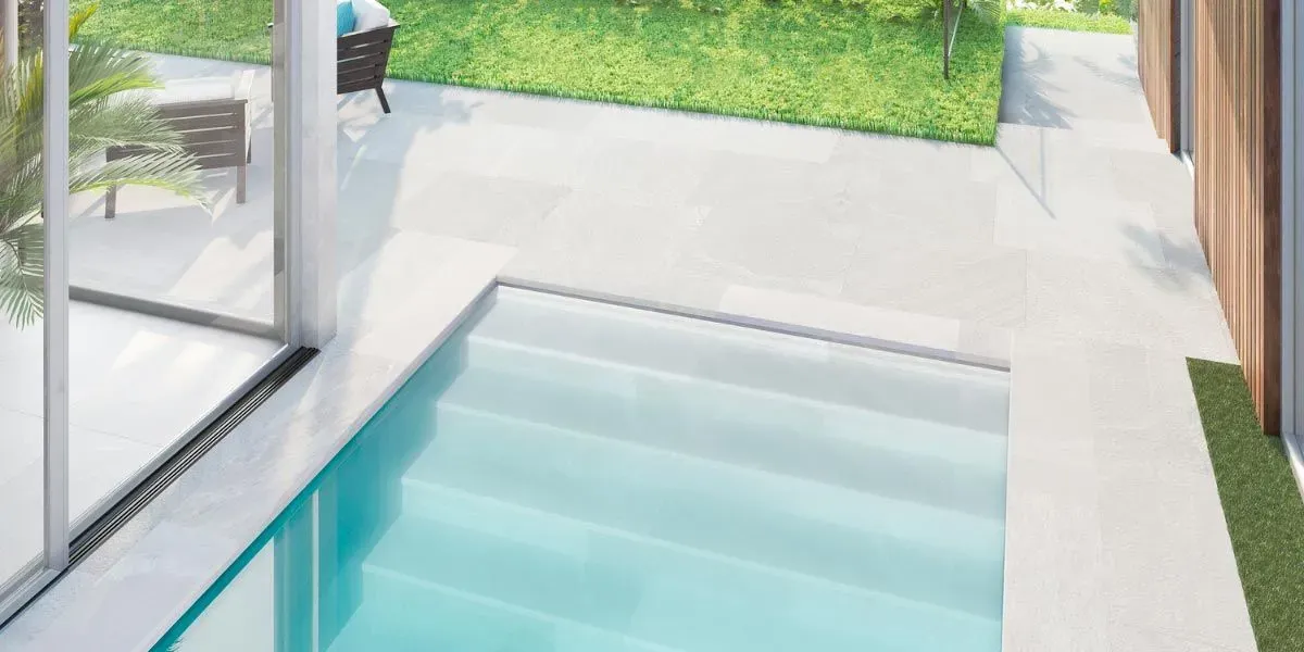 Piscina al aire libre con escalones incorporados, adyacente a una zona de césped y puertas corredizas de vidrio.