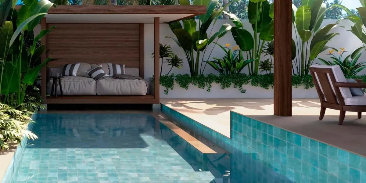 Piscina al aire libre con azulejos de color verde azulado y sofá cama de madera, con exuberante vegetación de fondo.