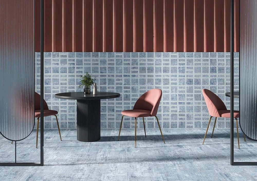 Interior del restaurante: mesa redonda con sillas rosas, contra paredes texturizadas azules y rojas, divididas por paneles de vidrio.