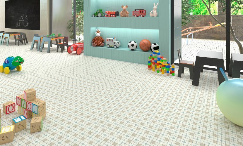 Sala de juegos con juguetes en estantes y en el suelo, mesas y sillas pequeñas, y una ventana que da a un patio de juegos.