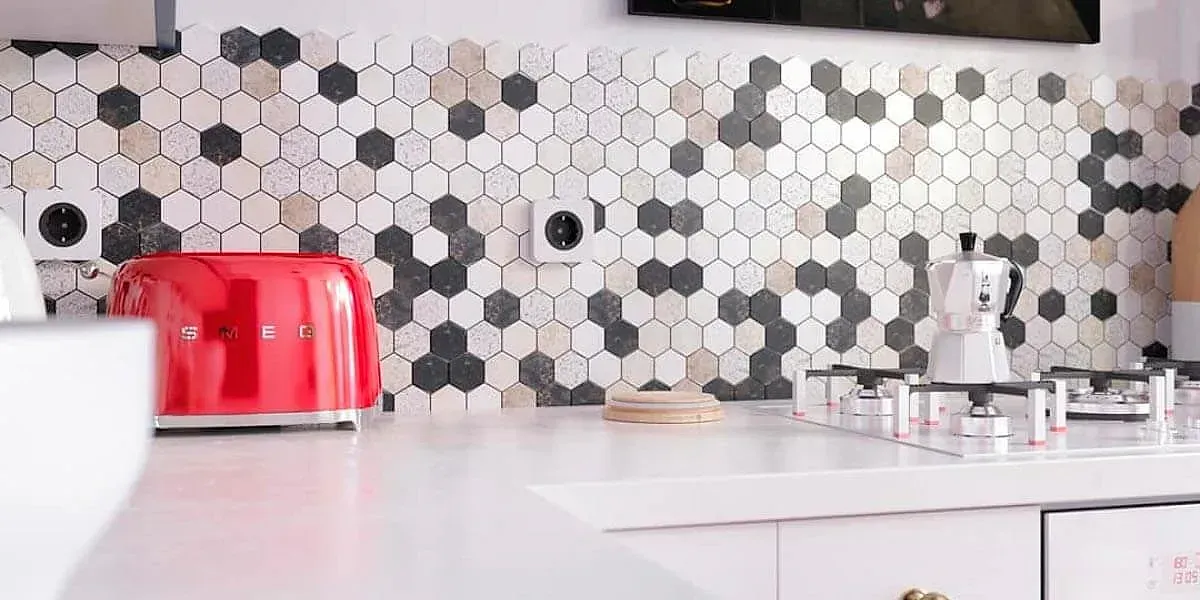 Tostadora roja sobre una encimera blanca en una cocina con salpicadero de azulejos hexagonales y una estufa.