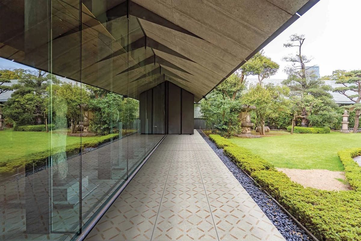Un edificio largo con paredes de cristal y un alero geométrico en el techo tiene vistas a un exuberante jardín verde.