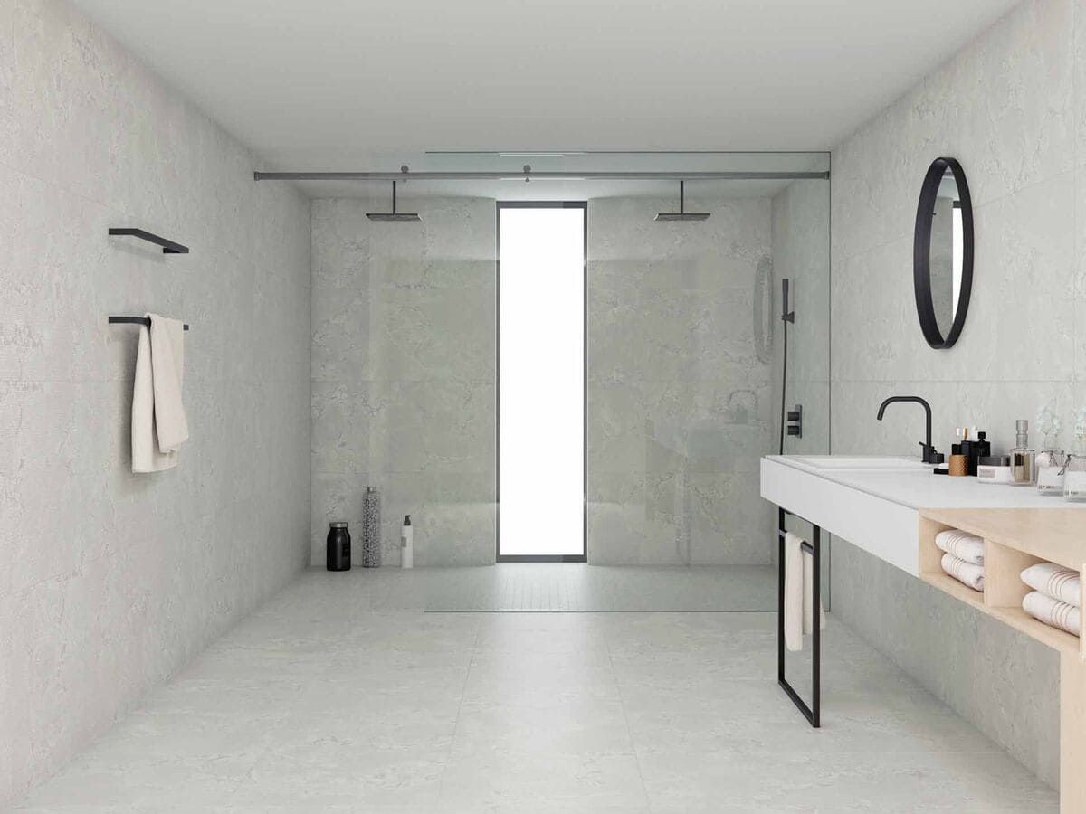 Baño moderno con ducha a ras de suelo. Paredes blancas, suelo de hormigón, grifería negra y lavabo largo.