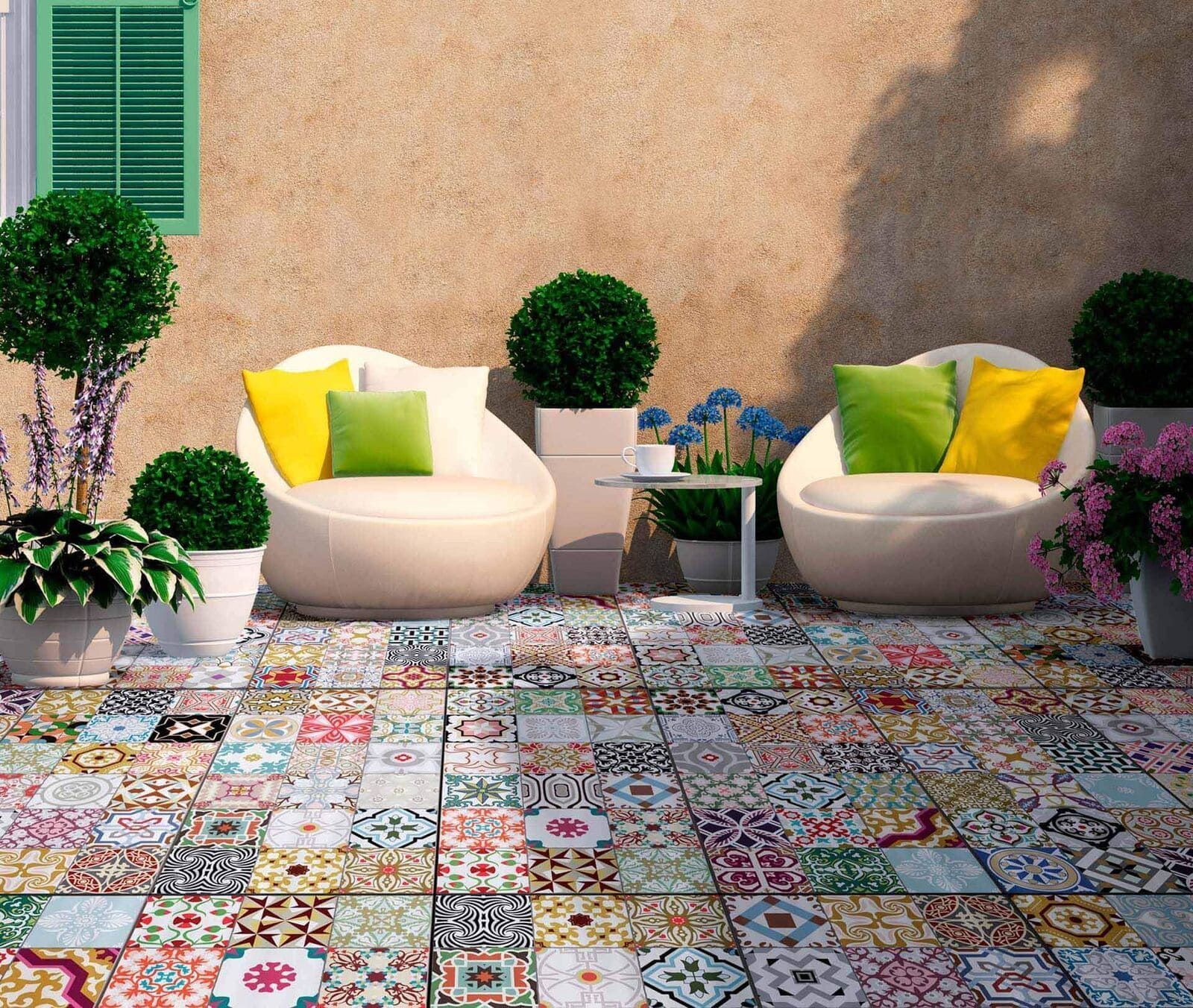 Patio con piso de baldosas con dibujos coloridos, sillones blancos con almohadas y plantas en macetas.