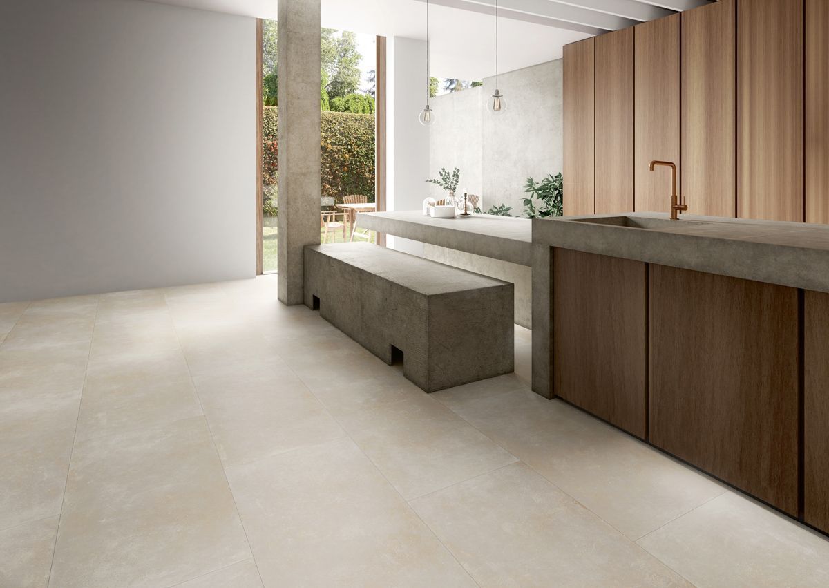 Cocina moderna con isla de concreto, gabinetes de madera y piso beige.