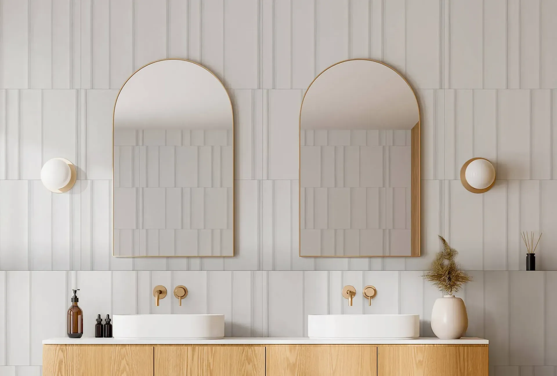 Baño con dos espejos arqueados, accesorios dorados y tocador de madera clara.