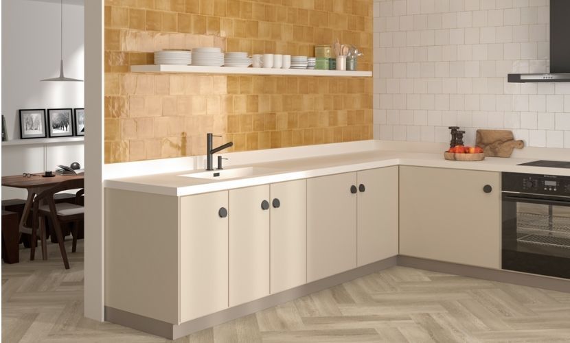 Una cocina con gabinetes claros y encimera blanca. Incluye fregadero, horno y estante con vajilla.