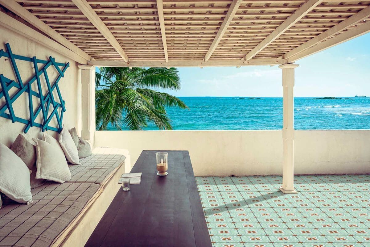 Patio en la azotea con vistas al océano. Decoración en azul claro y blanco, bancos con cojines y mesa de madera.