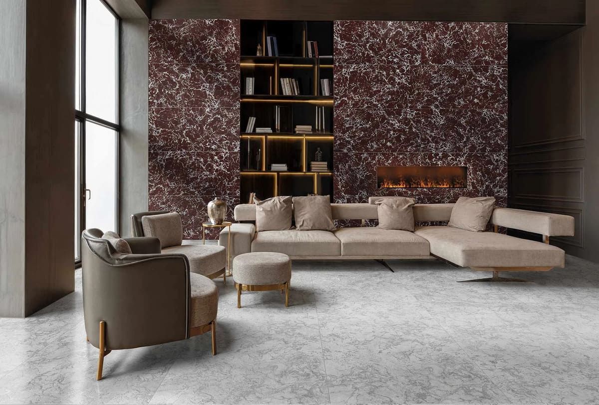 Sala de estar moderna con pared con acento burdeos, sofá y sillas beige, detalles dorados y una estantería.