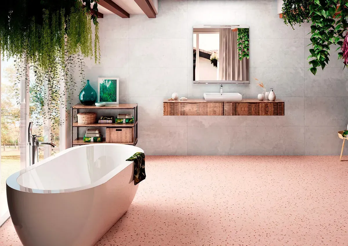 Baño moderno con bañera, tocador de madera y suelo moteado en rosa; vegetación cuelga del techo.