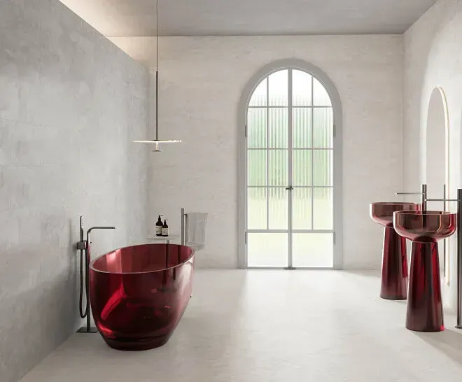Bañera roja y lavabos con pedestal en un baño blanco minimalista con ventana arqueada.