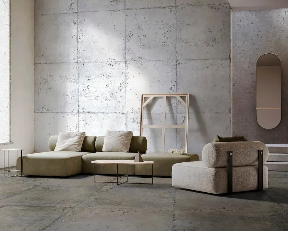 Sala de estar moderna con un sofá seccional verde, paredes de hormigón y decoración neutra.