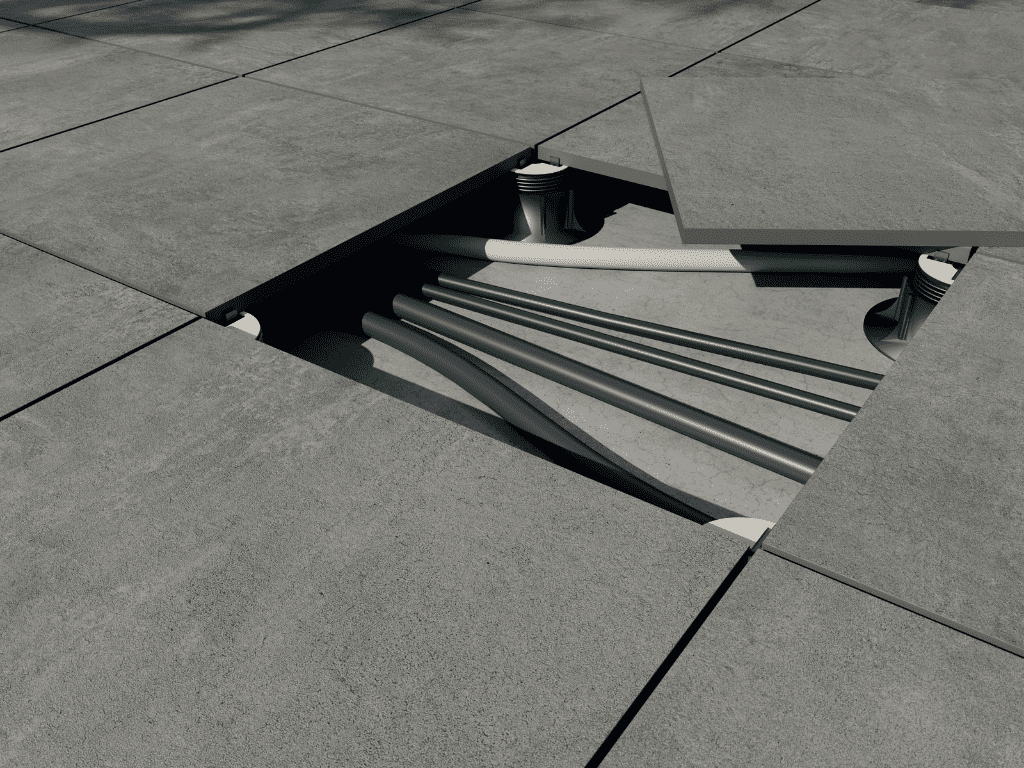 Baldosas grises del pavimento parcialmente retiradas, dejando al descubierto tuberías y soportes debajo.