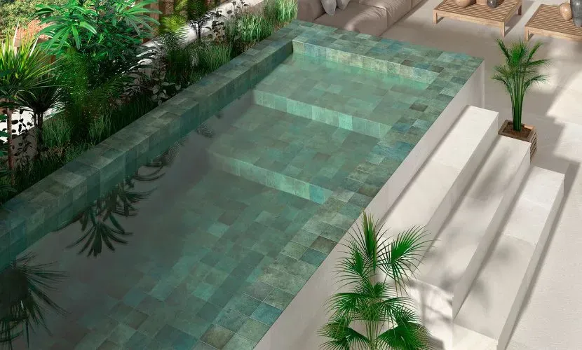 Piscina rectangular con azulejos turquesa y escalones. Palmeras y vegetación la rodean.