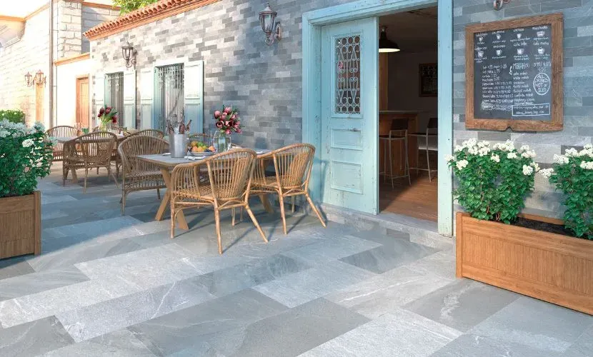 Patio de restaurante al aire libre con mesas, sillas y fachada de ladrillo, menú en pizarra y jardineras.