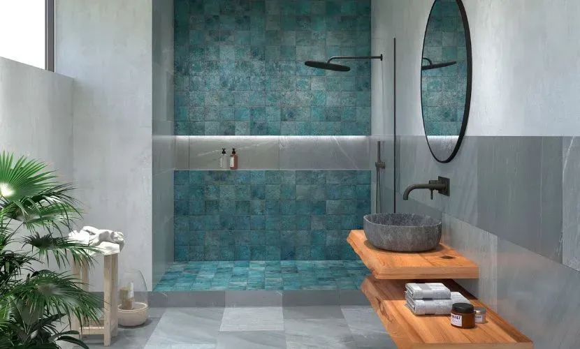 Baño con ducha con azulejos de color verde azulado, lavabo de piedra, tocador de madera y espejo grande.