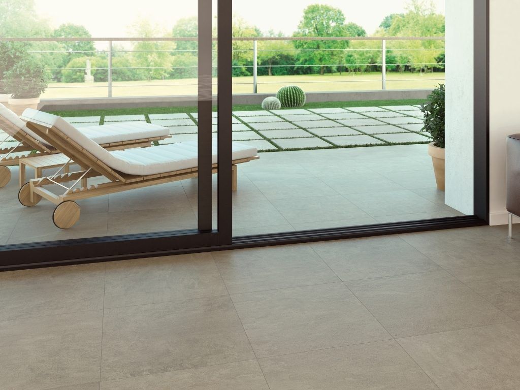 La puerta corrediza se abre a un patio con sillones, pisos de piedra y un jardín verde.