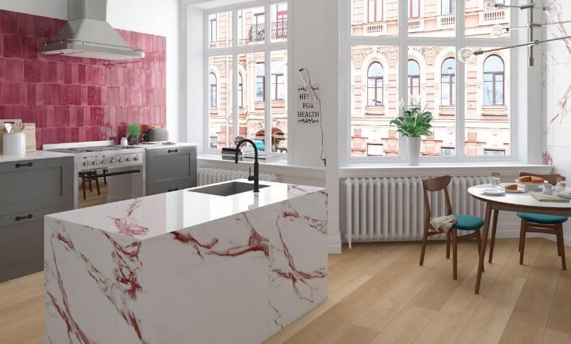 Cocina moderna con isla de mármol, suelo de madera y salpicadero rojo.