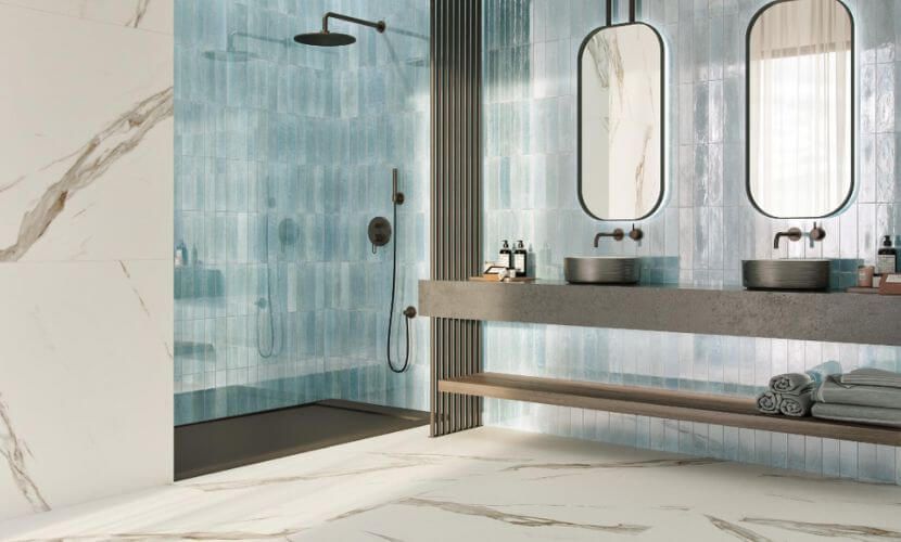 Baño moderno con ducha de azulejos azules, paredes de mármol y tocador doble.