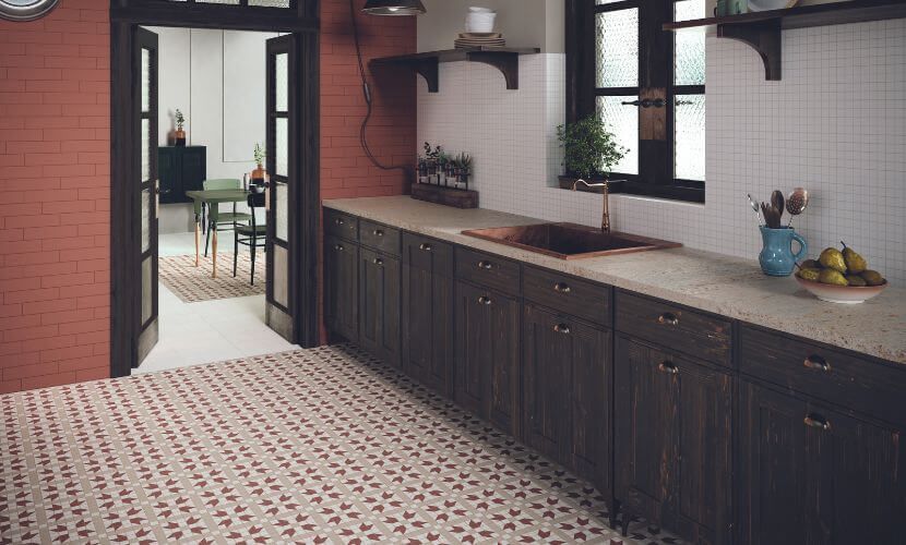 Cocina con gabinetes oscuros, pared de ladrillo rojo, piso estampado y puerta que conduce a un comedor.