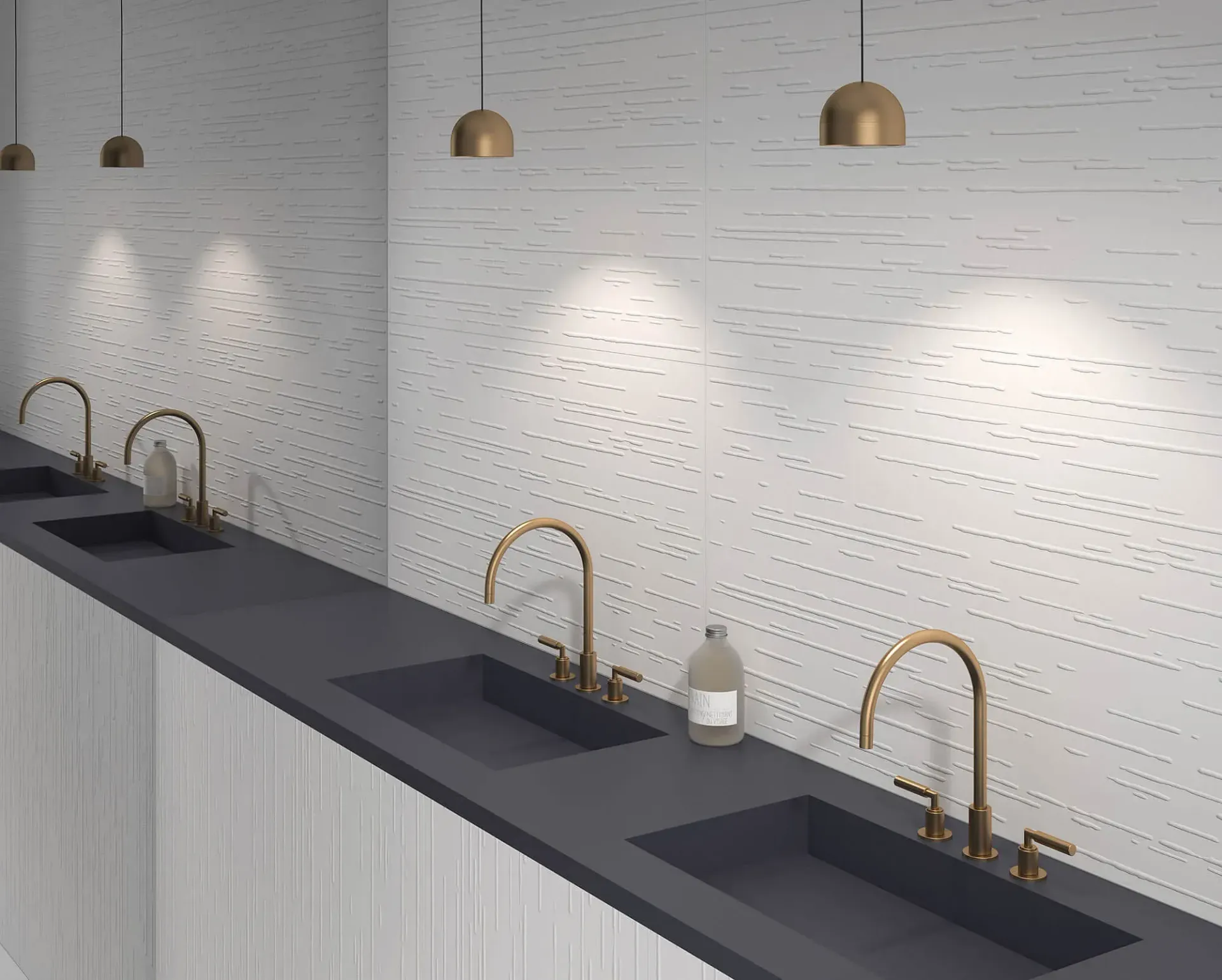 Baño público con lavabos, grifos dorados y luces colgantes sobre paredes blancas texturizadas.