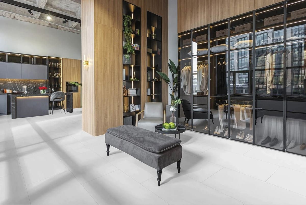 Vestidor moderno con puertas de vidrio, detalles de madera y una zona de estar con banco y sillón.