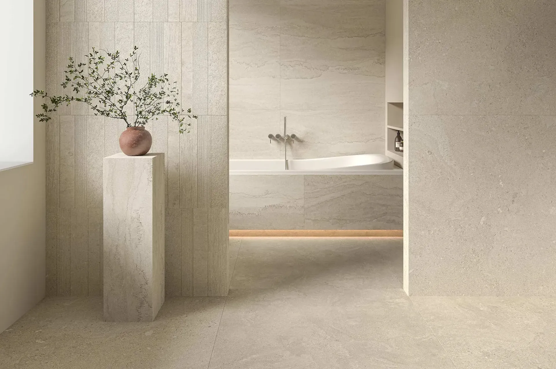 Baño beige con azulejos de piedra, un jarrón de pedestal y una bañera al fondo.