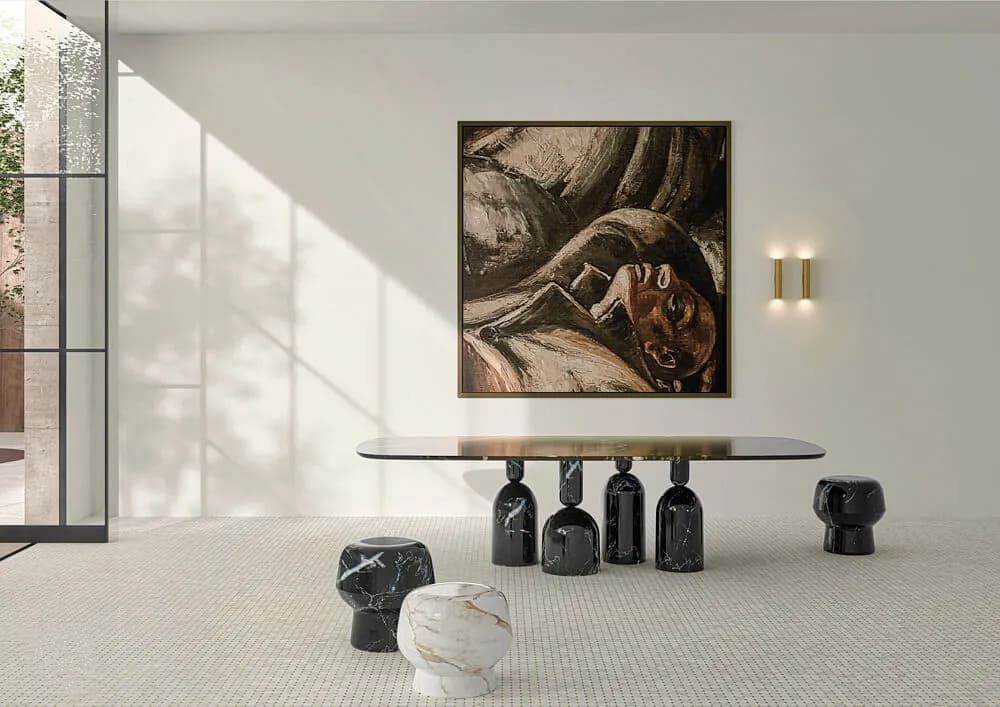 Comedor moderno con mesa larga, taburetes de mármol y obras de arte en una pared blanca.