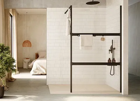 Baño moderno con ducha abierta, marco negro, azulejos blancos, toallero, cabezal de ducha y una vista del dormitorio.