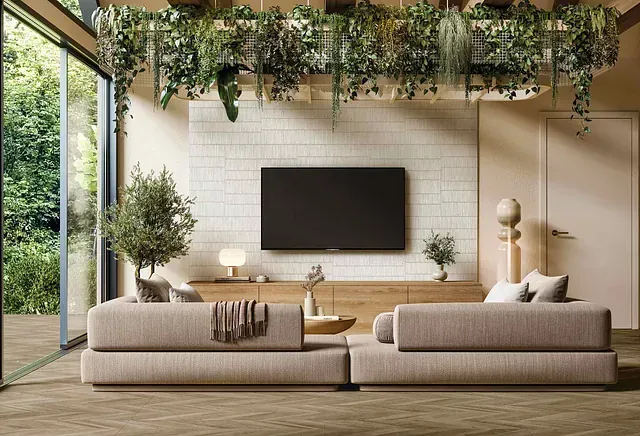 Sala de estar con grandes ventanales, sofá modular beige, TV, consola de madera, plantas y vegetación colgante.